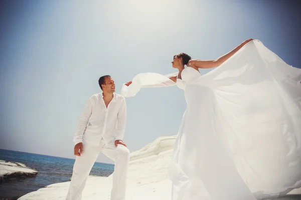 Wind blaast jurk van de bruid terwijl ze achter een bruidegom op een se staat — Stockfoto