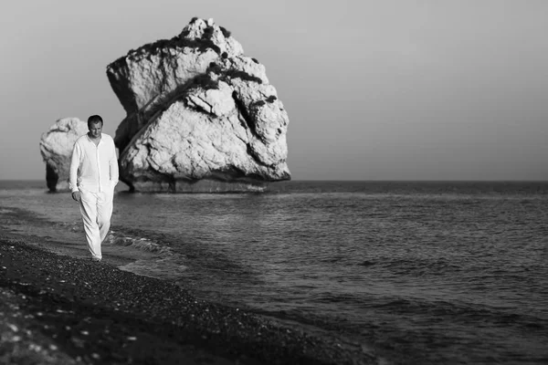 Чоловік у білій сорочці і штани ходять уздовж берега моря подумав — стокове фото