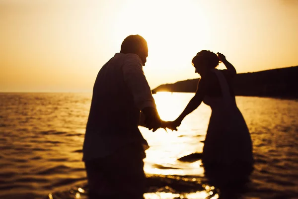 Bruden och brudgummen promenera i vattnet till solnedgången — Stockfoto