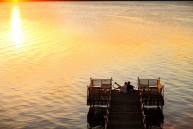 Gelin ve damat köprüde bir deniz üzerine arka arkaya oturmak 