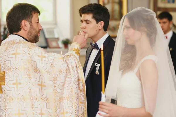 Noivo beija uma aliança de casamento realizada por um padre — Fotografia de Stock