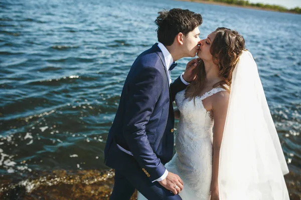 Fidanzato baci sposa teneramente in piedi con lei in riva al mare — Foto Stock