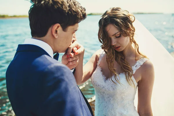 Bräutigam küsst die zarte Hand der Braut, während der Wind ihr Haar weht — Stockfoto