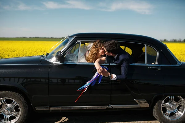 Ein zärtlicher Kuss lustiger Frischvermählter, die in einem alten Auto sitzen und — Stockfoto