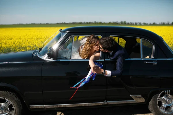 Novio besa a una novia que llega a ella desde el asiento trasero de un coche — Foto de Stock