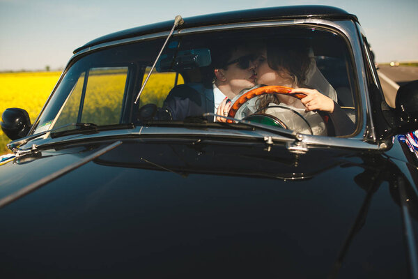 Groom kisses a bride while she drives an old car 