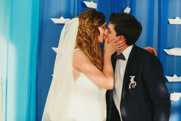 Novia sostiene la cara del novio durante un beso detrás de una pared de tela azul —  Fotos de Stock