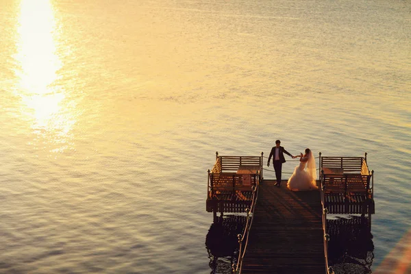 Happy wedding couple stands on the end of a bridge over the sea — Stock Photo, Image