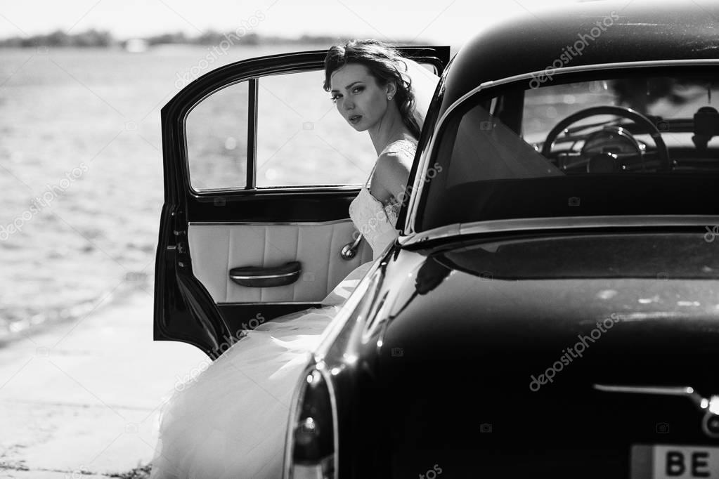 Bride sits in an open car while wind blows around it 