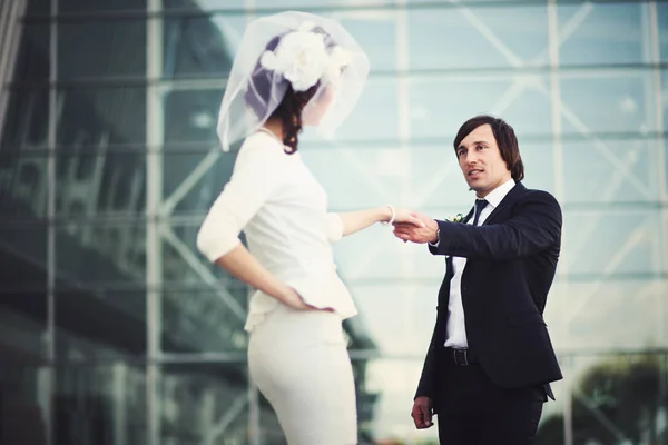 Handsome groom holds bride's hands posing in the front of glass — Stock Photo, Image