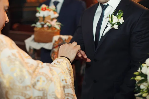 Священник нежно надевает обручальное кольцо на руку жениху — стоковое фото