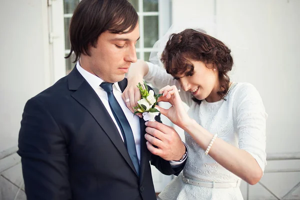 Pretty bride looks funny while adjusting a boutonniere on groom' — Stockfoto
