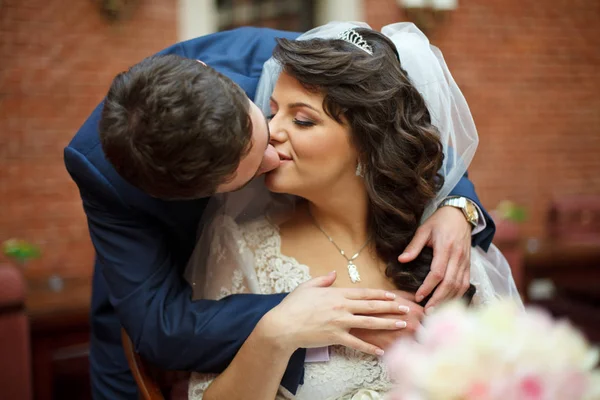 Жених нежно целует невесту, пока она сидит за столом — стоковое фото