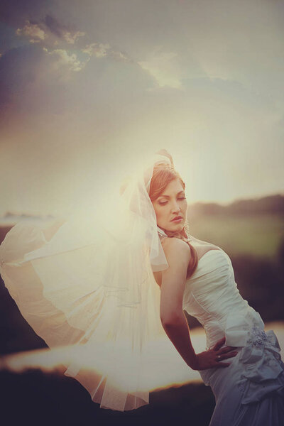 Bride bends over standing in the rays of evening sun
