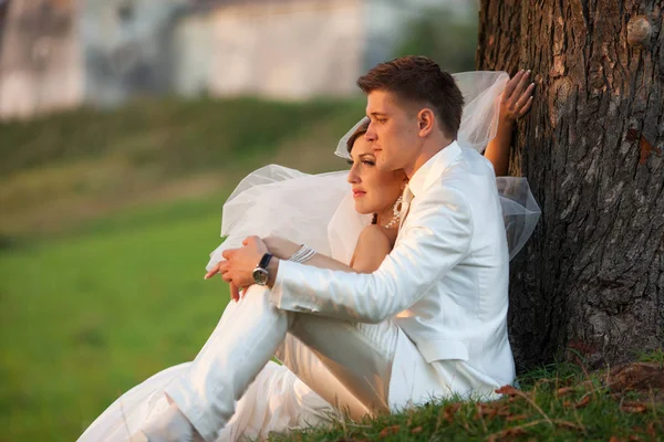 Le voile de la mariée explose alors qu'elle est assise avec un marié sur l'herbe — Photo