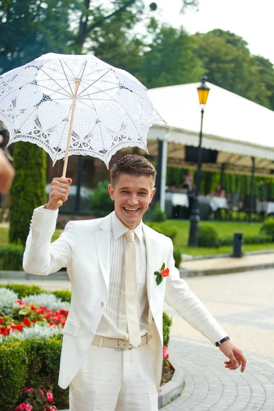 신랑은 흰 양복 미소 레이스 우산을 들고 있습니다 — 스톡 사진