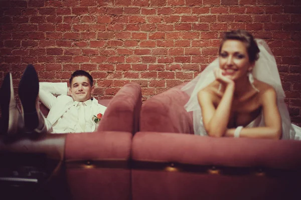 Os recém-casados felizes descansam nos sofás vermelhos — Fotografia de Stock