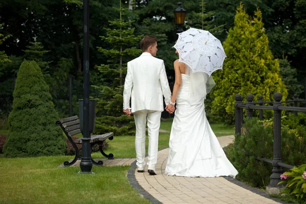 Pengantin pria dalam setelan putih memegang tangan pengantin saat berjalan di gard — Stok Foto