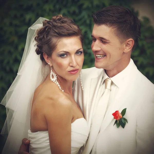 Smiling groom hugs a stunning bride posing in the front of a wal — Stock Photo, Image