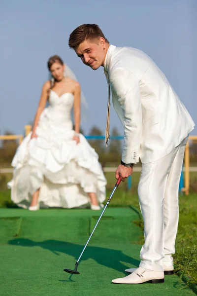 新郎穿白衣服打高尔夫球，而新娘站在背景上 — 图库照片