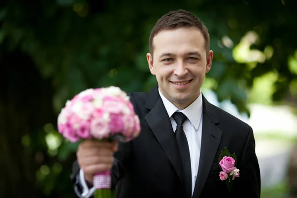 Sorridente sposo tiene bouquet da sposa in piedi fuori — Foto Stock