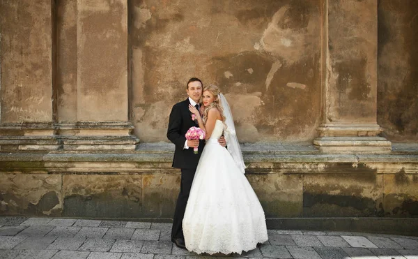Нежная невеста наклоняется к жениху, стоящему у старой стены — стоковое фото