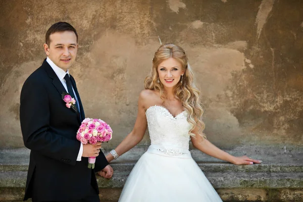 Sposo tiene un bouquet da sposa rosa in piedi dietro una sposa — Foto Stock