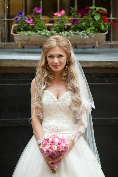 Winzige blonde Braut steht unter der Fensterbank voller Blumen — Stockfoto