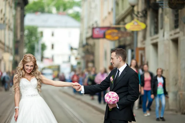 Bruden och brudgummen nå sina händer som poserar på spårvägen — Stockfoto