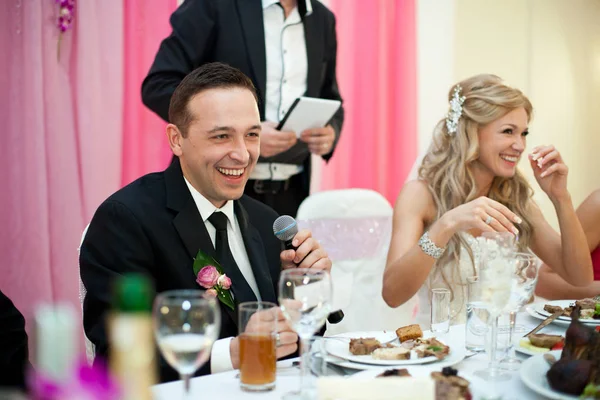 Смеющийся жених держит микрофон, сидя за невестой — стоковое фото