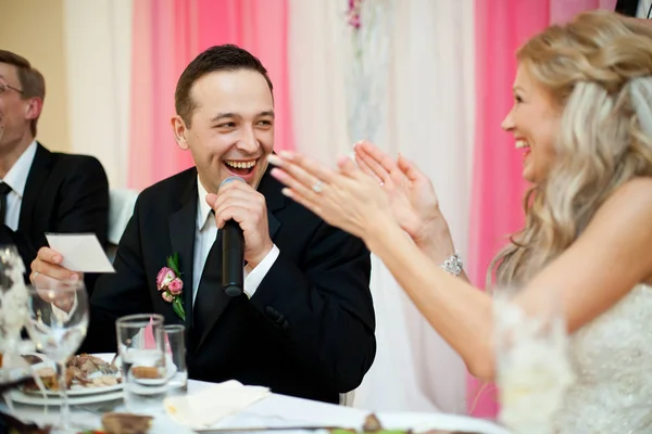 Смеющаяся невеста аплодирует сидящему за женихом — стоковое фото