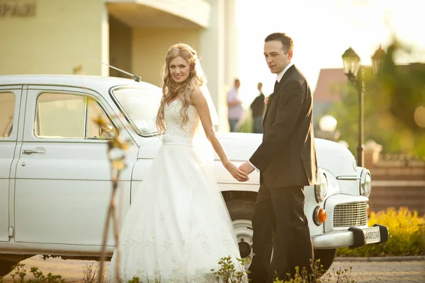 Bruid loopt achter een oude auto die bruidegom hand — Stockfoto