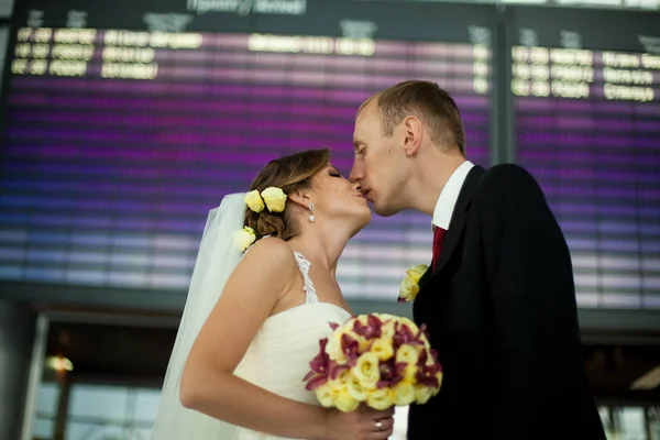 Recém-casados beijam-se em pé na sala do aeroporto — Fotografia de Stock