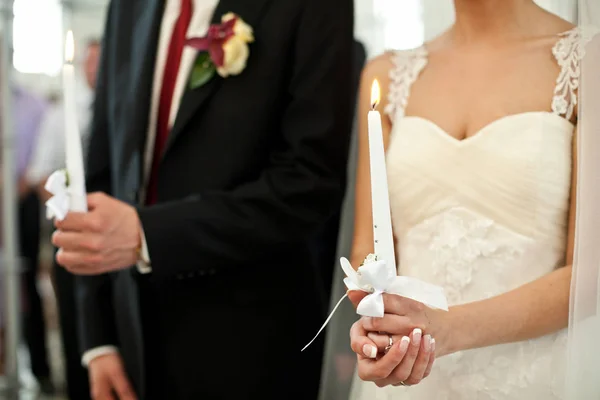 Крупный план горящих свечей, удерживаемых женихом и невестой — стоковое фото