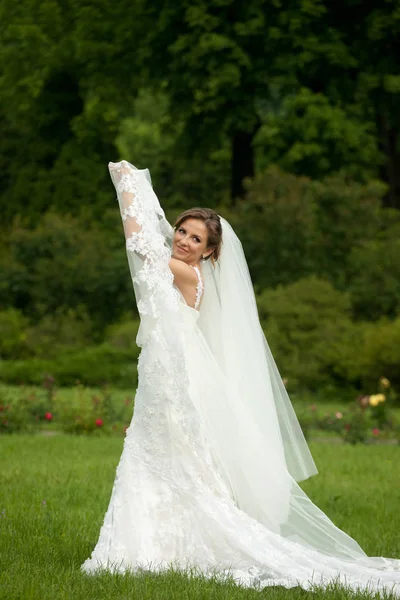 花嫁は、緑の芝生の上に立ってを彼女のベールを発生させます — ストック写真