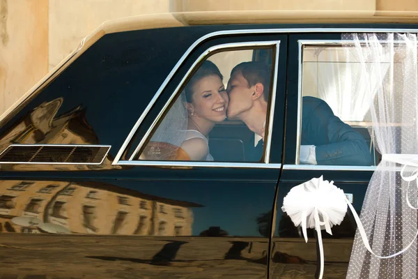 Novia sonríe mientras el novio la besa sentada en la limusina — Foto de Stock