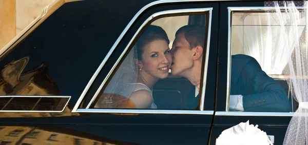 Noivo beija bochecha da noiva sentado na limusine — Fotografia de Stock