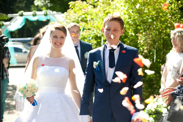 Os convidados jogam pétalas no casal de casamento sorridente andando para o — Fotografia de Stock