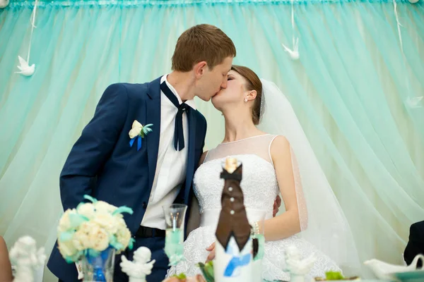 Noiva e noivo beijam de pé na mesa de jantar na frente o — Fotografia de Stock