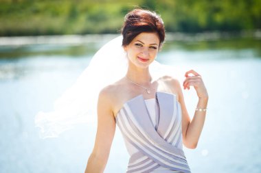 Mor bir elbise içinde gülümseyen gelin bir göl ön tarafında teşkil etmektedir.