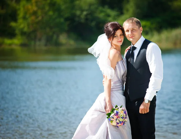 Bräutigam umarmt Braut zart, die vor einem See steht — Stockfoto