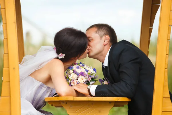 Bruid en bruidegom kussen zitten in de houten cabine — Stockfoto