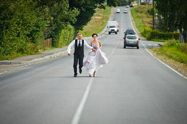 Szczęśliwy ślub para biegnie autostrada — Zdjęcie stockowe
