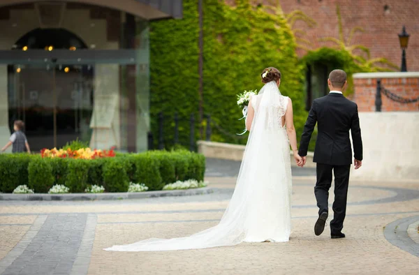 Bruid en bruidegom in zwart pak lopen rond de bloem-bed — Stockfoto