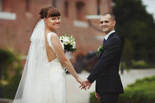 Lachende bruid kijkt over haar schouder bezit bruidegom hand — Stockfoto