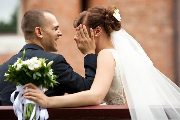 Le marié riant tient le visage de la mariée assis sur le banc — Photo