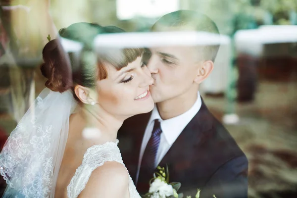 Luz brilha no vidro, enquanto os recém-casados se beijam atrás dele — Fotografia de Stock