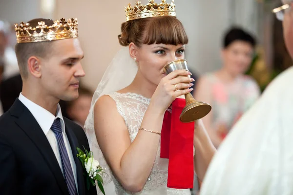 Улыбающаяся невеста пьет священное вино, стоя перед священником — стоковое фото