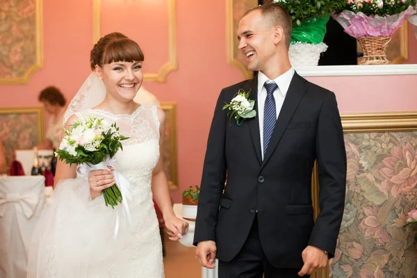 Uśmiechający się nowożeńcy stoją w sali hotelu różowy — Zdjęcie stockowe