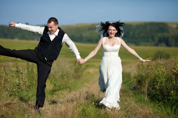 Vento sopra cachos negros da noiva, enquanto o noivo pula atrás dela — Fotografia de Stock